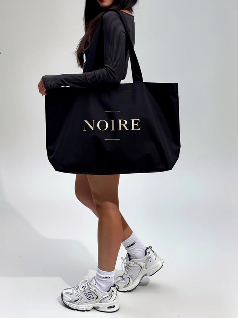 Woman carrying Noiré logo statement canvas tote bag black lifestyle side view