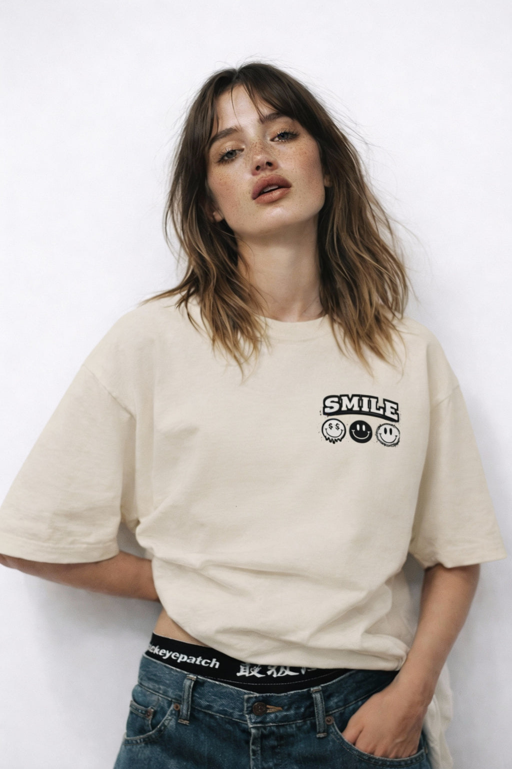 Model wearing beige t-shirt with small “Smile” chest graphic, casual modern streetwear outfit by Noiré.
