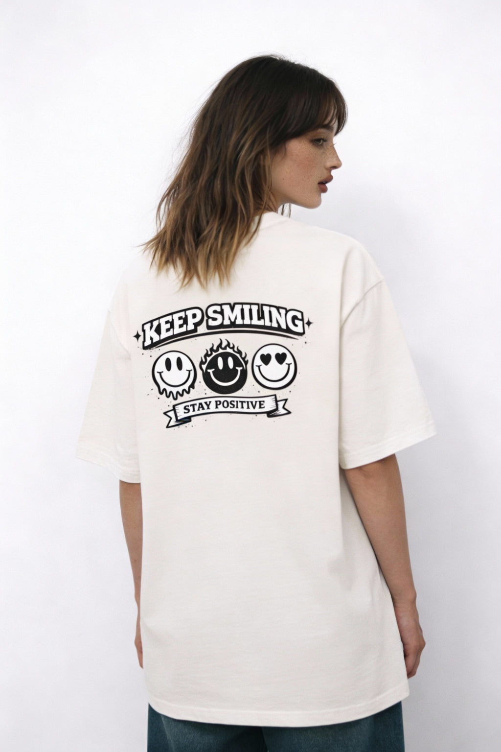 Model wearing beige t-shirt showing “Keep Smiling – Stay Positive” back print with smiley faces, creative streetwear look by Noiré.