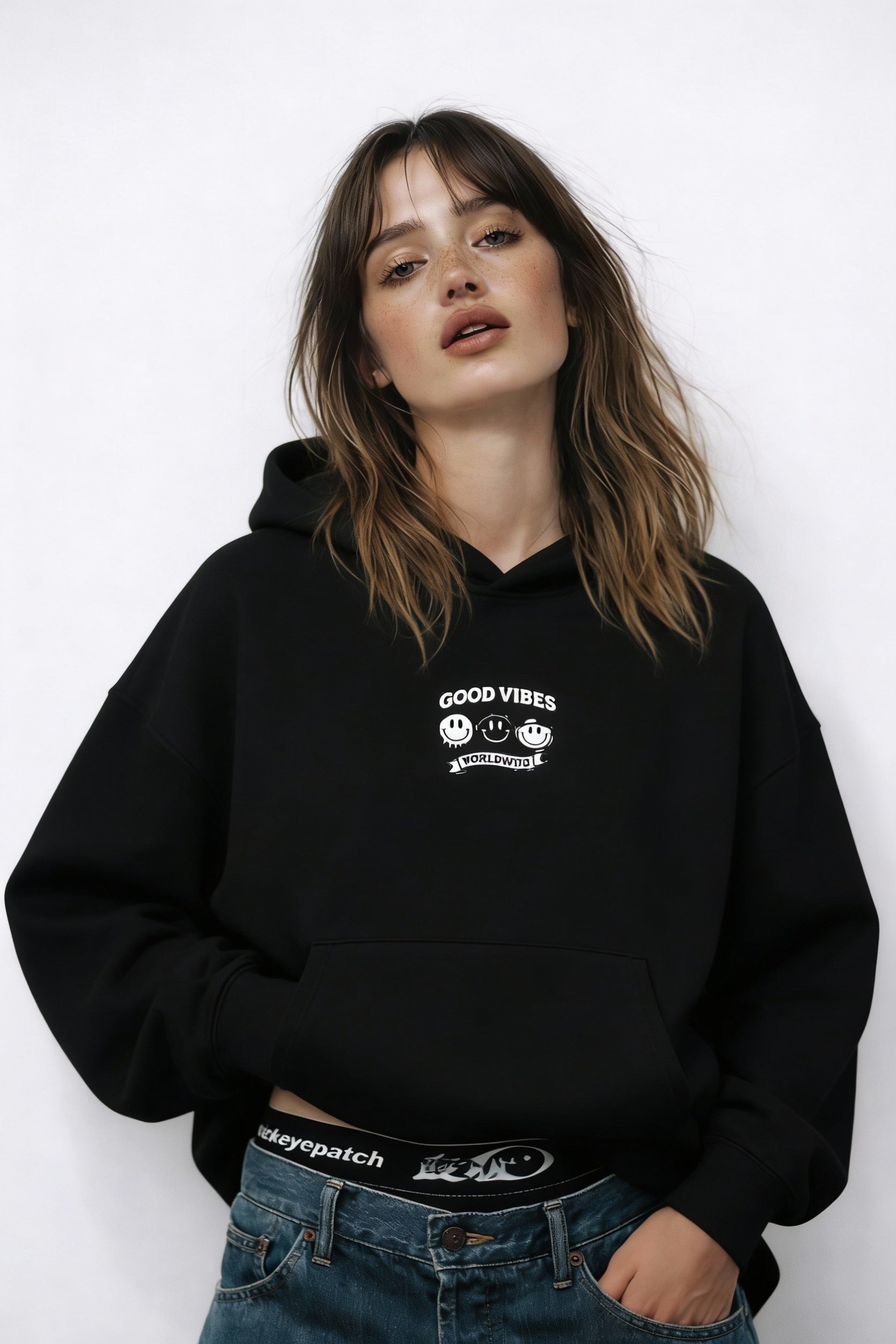 Noiré black oversized streetwear hoodie front view with “Good Vibes Worldwide” smiley graphic print, worn by female model, unisex graphic hoodie.