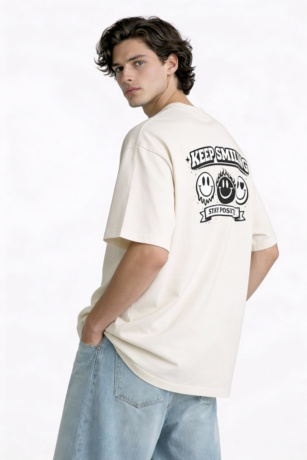 Model wearing beige t-shirt showing “Keep Smiling – Stay Positive” back print with smiley faces, creative streetwear look by Noiré.