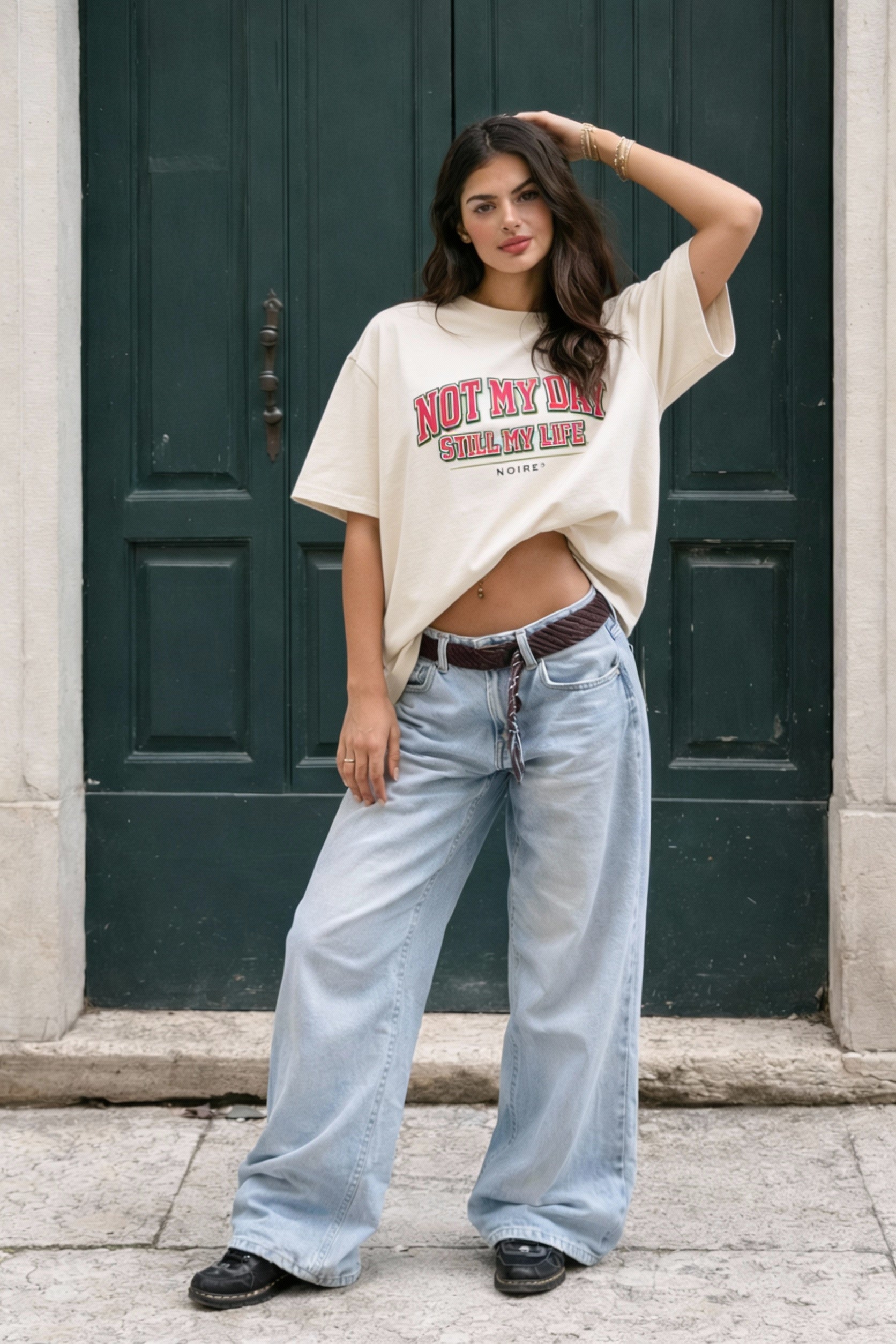 Female model wearing beige oversized t-shirt with red vintage typography print, casual streetwear look by Noiré.