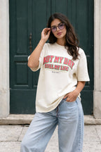 Female model in beige oversized t-shirt with red vintage lettering, everyday streetwear style by Noiré.