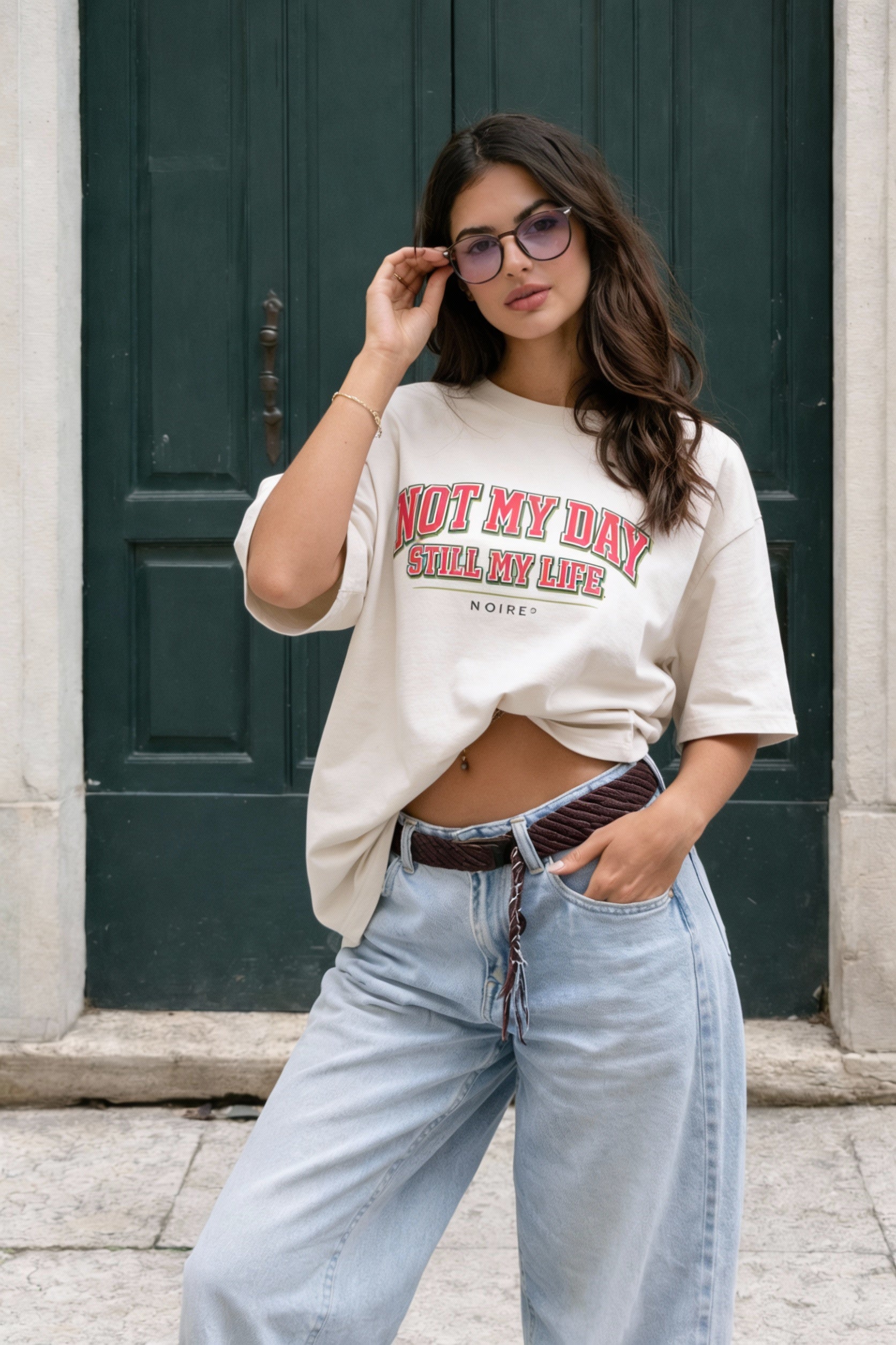 Female model posing in beige oversized t-shirt with red retro text graphic, relaxed urban outfit by Noiré.
