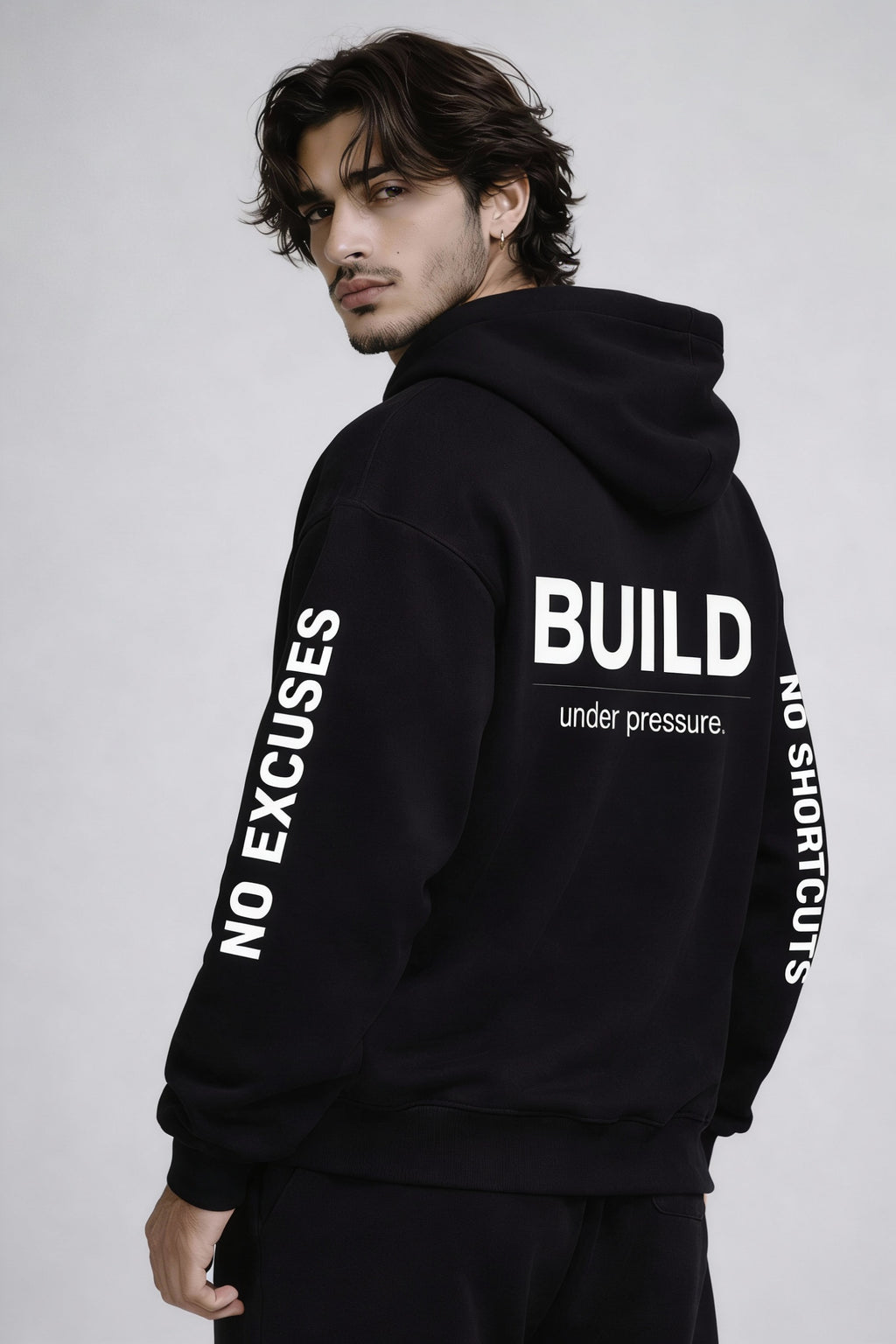 Noiré black hoodie back view with bold white “BUILD under pressure.” graphic and sleeve text “No Shortcuts” – oversized streetwear hoodie