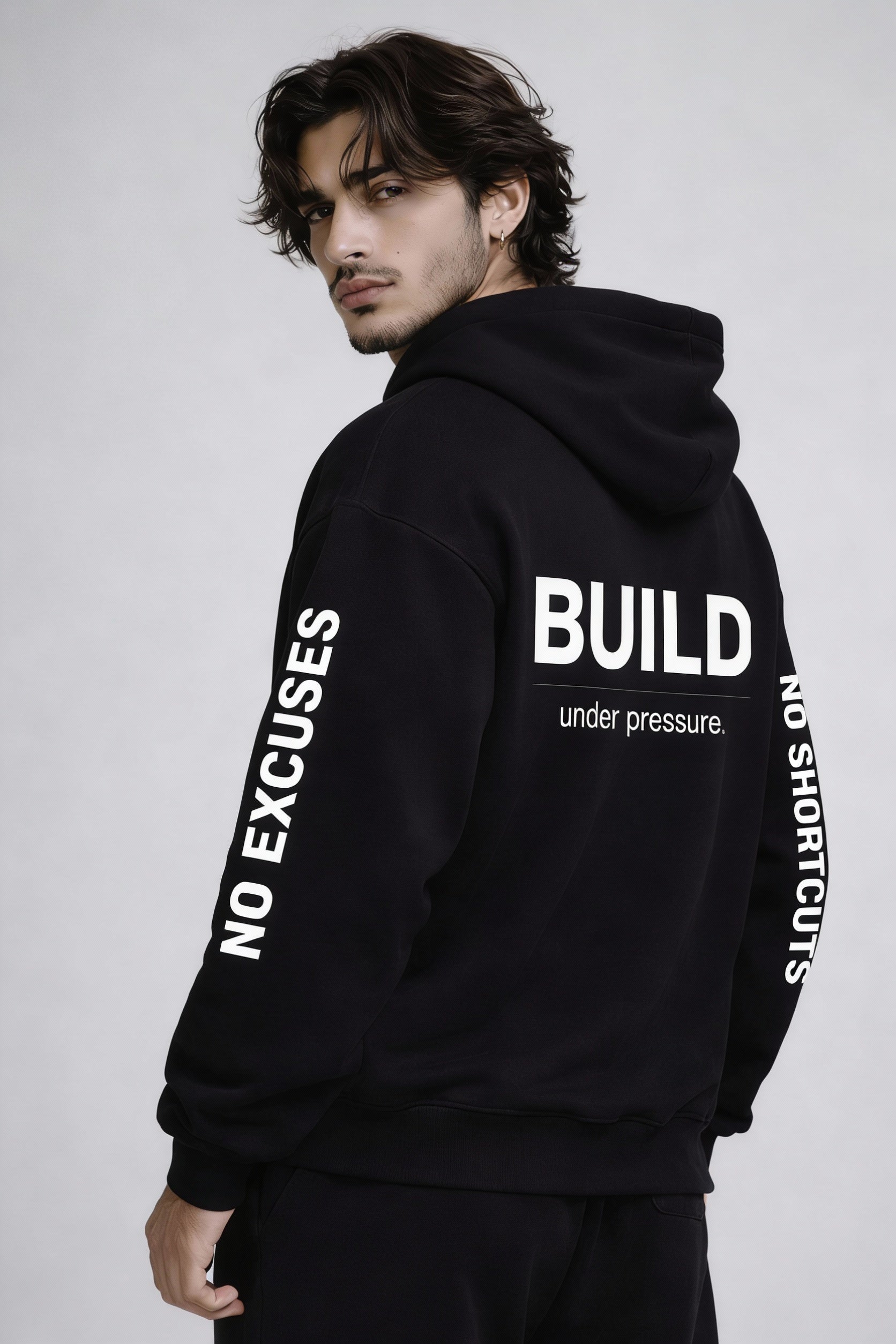 Noiré black hoodie back view with bold white “BUILD under pressure.” graphic and sleeve text “No Shortcuts” – oversized streetwear hoodie