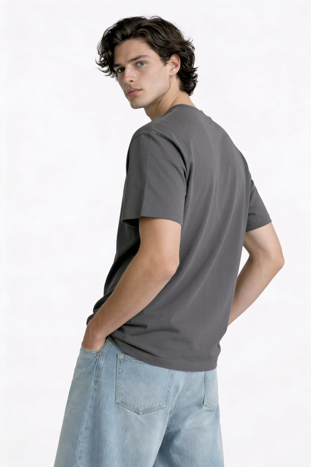 Male model wearing oversized dark grey t-shirt shown from the back, relaxed fit with clean minimalist design, modern streetwear by Noiré.