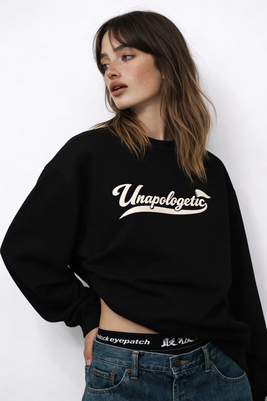 Noiré Unapologetic black oversized sweatshirt, front view on female model, cream script logo, streetwear
