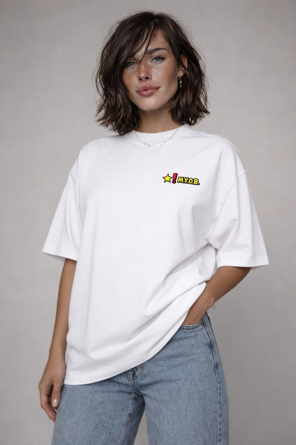 White oversized graphic T-shirt with small “MYOB” chest logo and star icon, worn by female model, minimalist streetwear look