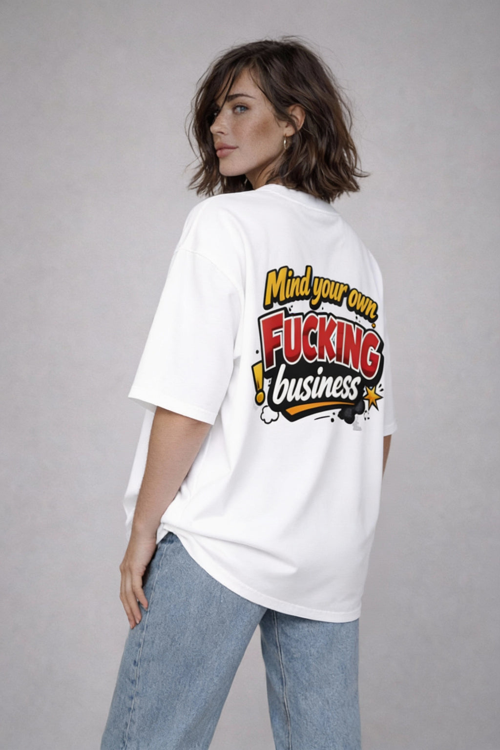 Back view of white oversized T-shirt with bold “Mind Your Own F*cking Business” graffiti typography graphic, streetwear statement design on female model