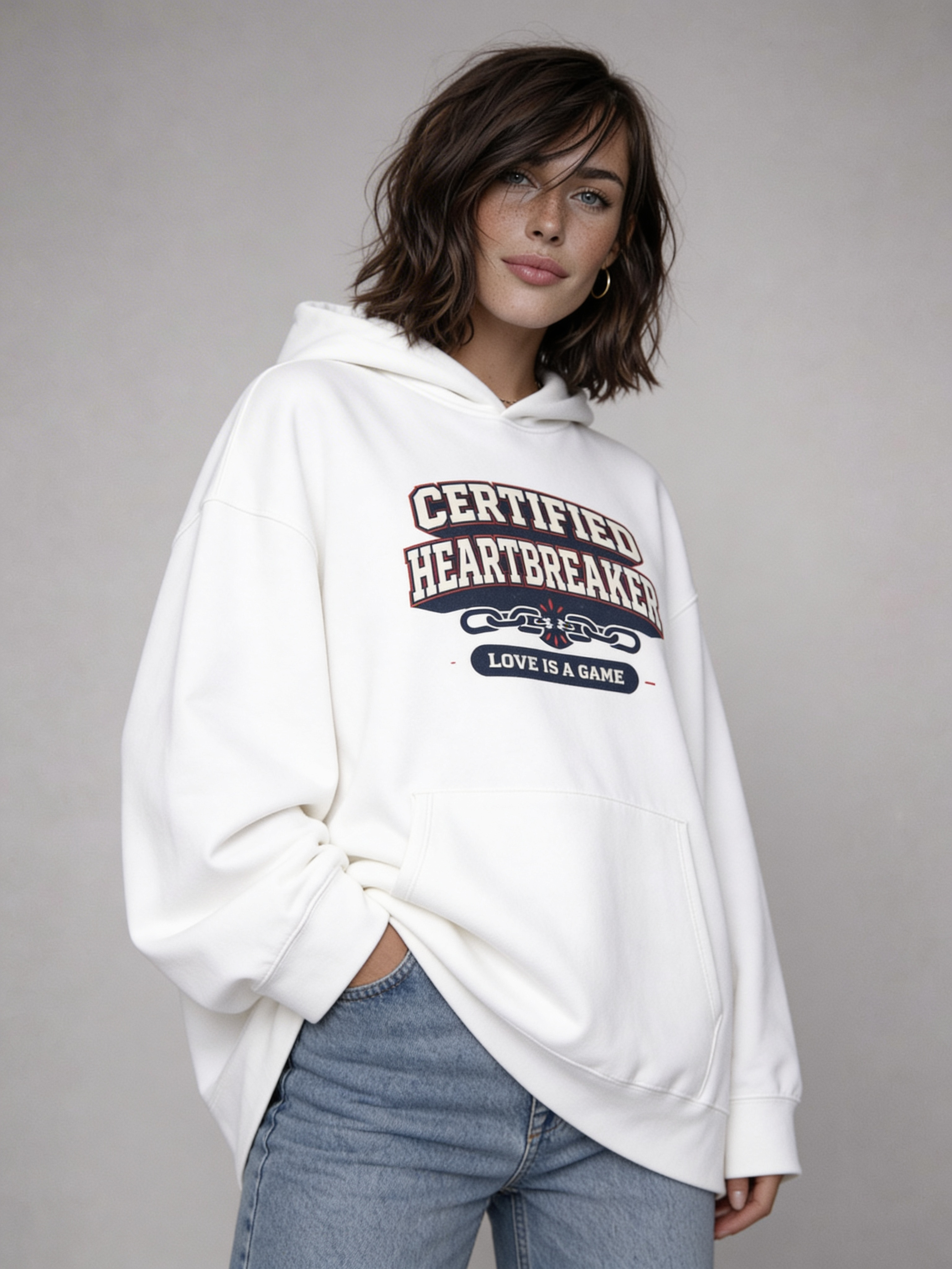 Noiré white oversized hoodie front view with “Certified Heartbreaker – Love Is a Game” bold varsity print, worn by female model, unisex streetwear hoodie.