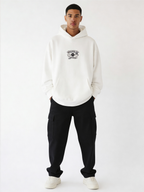 Noiré white oversized streetwear hoodie front view with “Good Vibes Worldwide” smiley logo print, worn by male model, unisex streetwear hoodie.