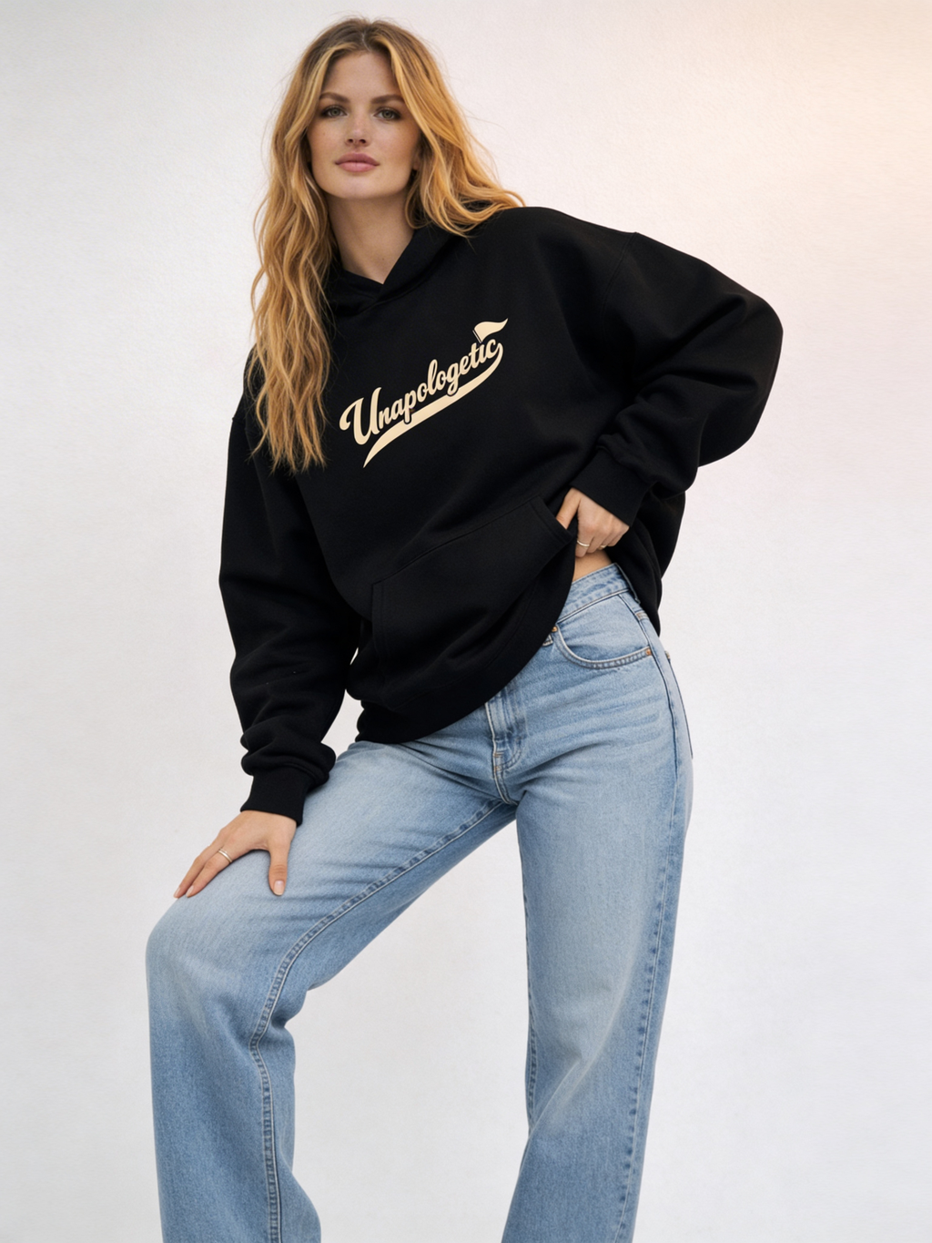 Noiré black oversized streetwear hoodie front view with “Unapologetic” script graphic in beige, worn by female model, unisex statement hoodie.