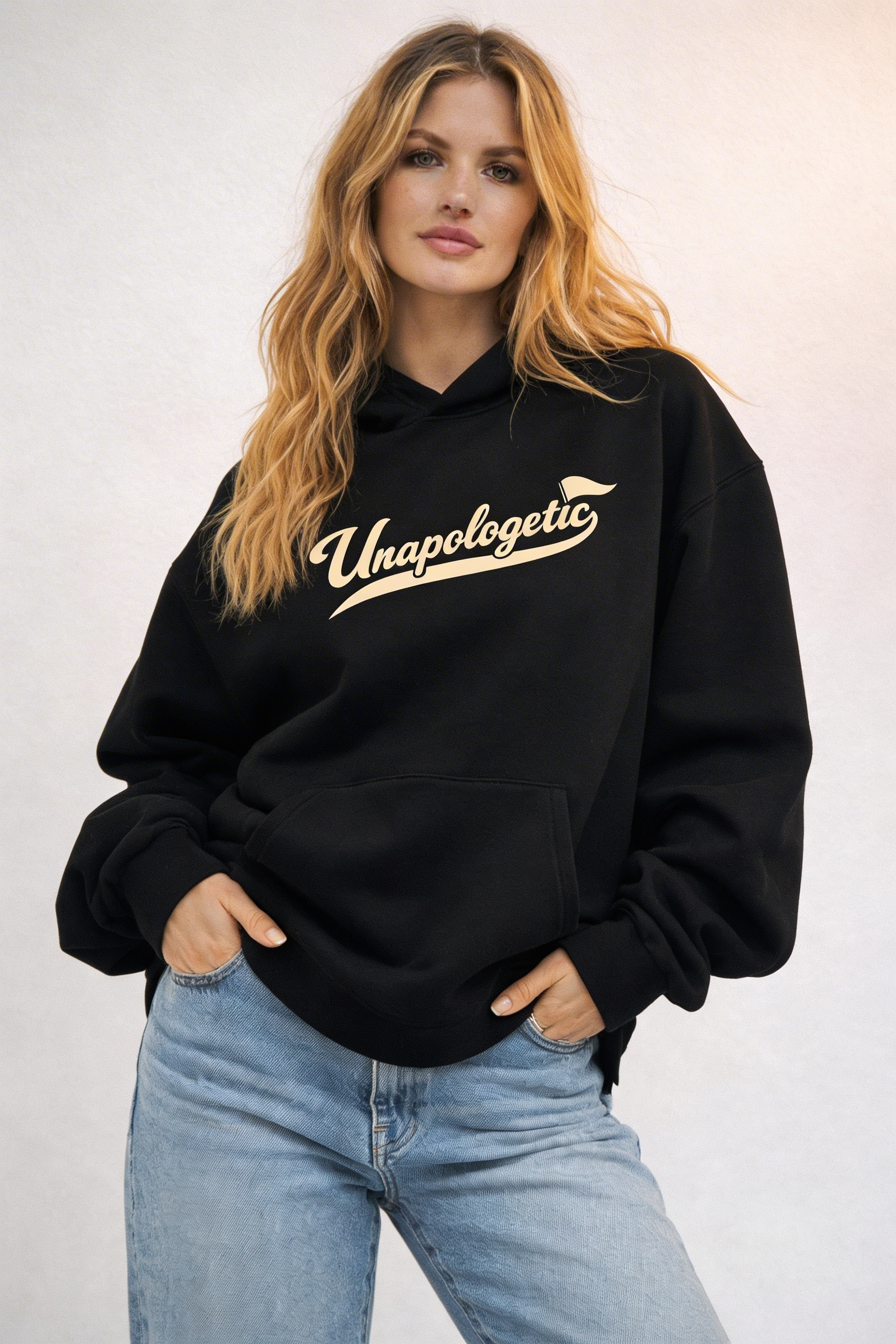 Noiré black oversized streetwear hoodie front view with “Unapologetic” script graphic in beige, worn by female model, unisex statement hoodie.