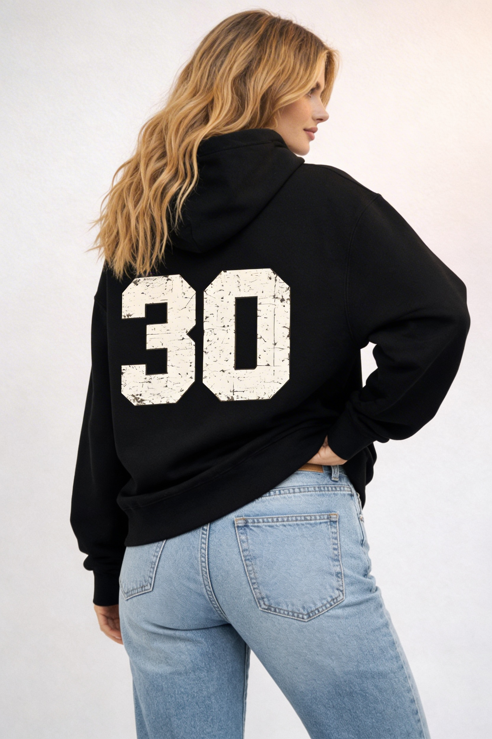 Noiré black oversized streetwear hoodie back view with large distressed “30” varsity number print, worn by female model, urban graphic hoodie.