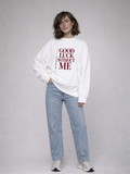 Female model wearing white oversized Noiré sweatshirt with “Good Luck Without Me” graphic, front full-body studio shot, light wash jeans.