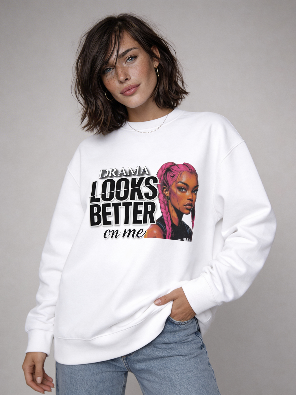 White oversized sweatshirt with “DRAMA LOOKS BETTER ON ME” graphic and pink braided illustration, angled studio view highlighting front design.