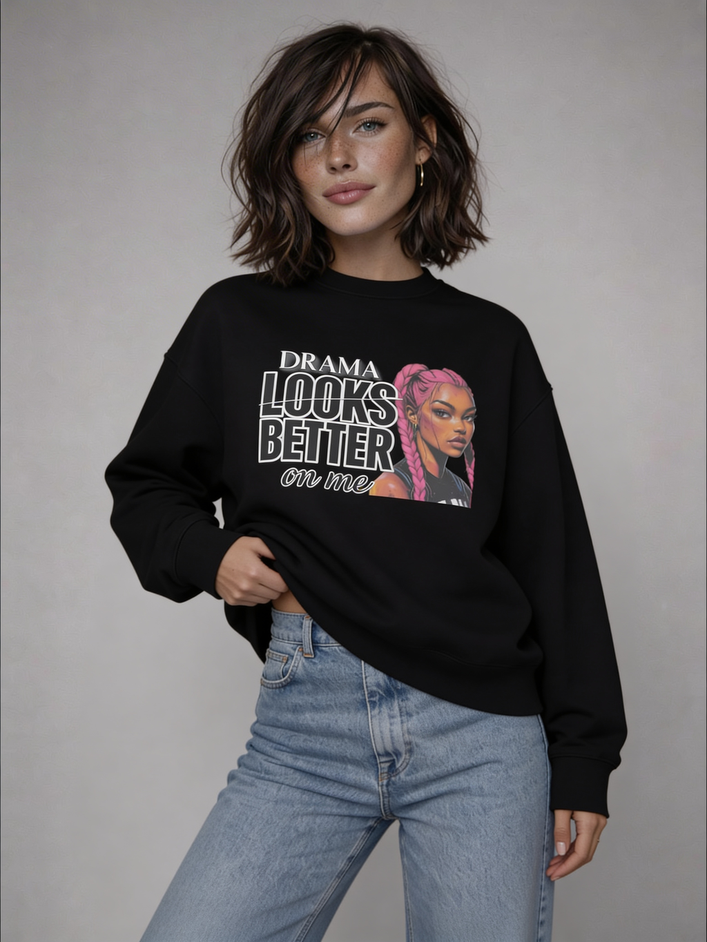 Black oversized sweatshirt with “DRAMA LOOKS BETTER ON ME” graphic and pink braided illustration, worn by female model with light blue jeans, front studio shot.
