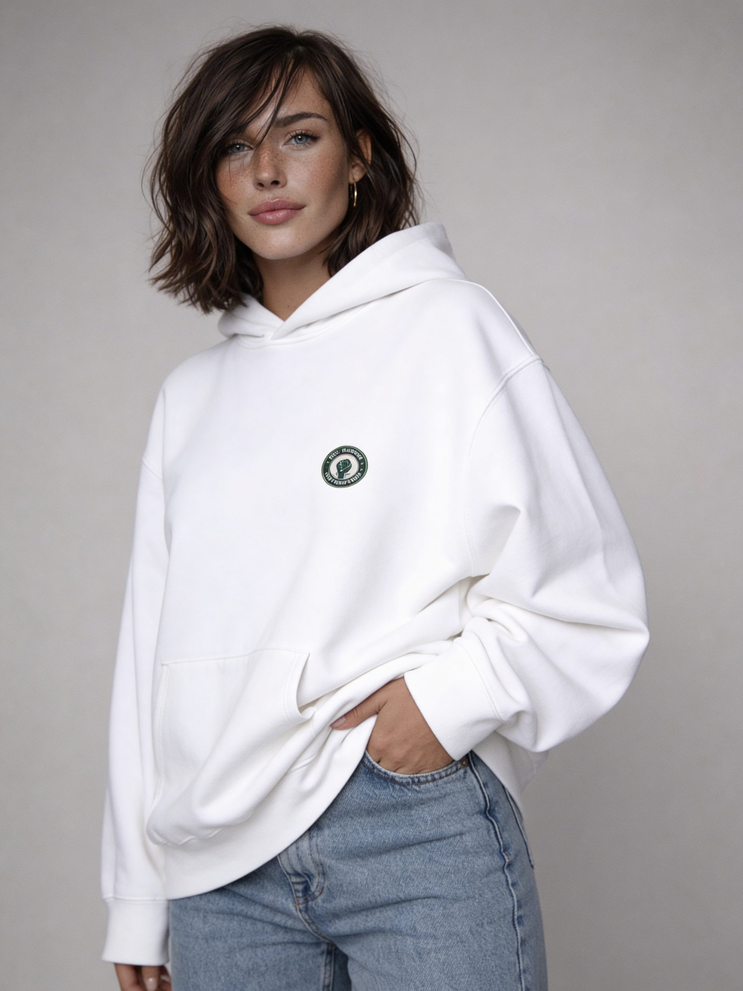 White oversized hoodie front view on female model wearing light blue jeans, minimal streetwear style