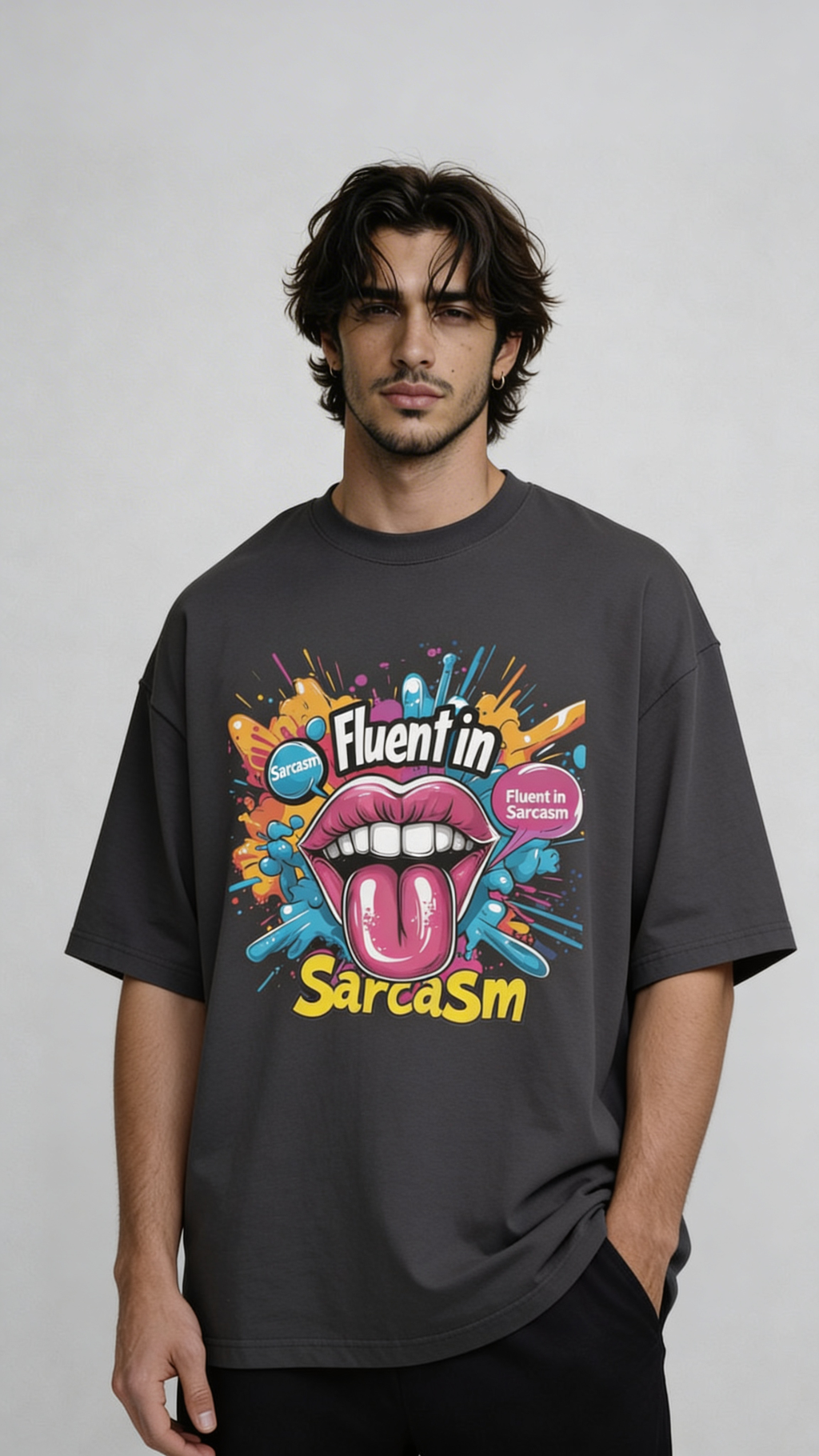 Male model wearing oversized dark gray “Fluent in Sarcasm” t-shirt with bold multicolor graphic print and casual streetwear styling.