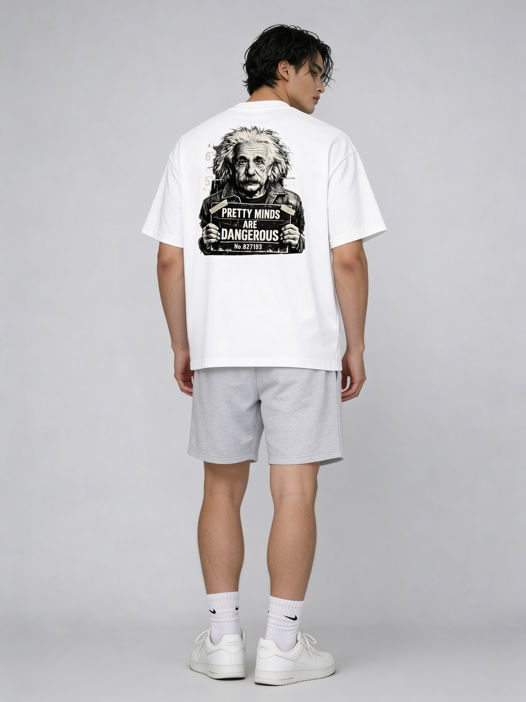 Young male model in oversized white graphic tee featuring Albert Einstein mugshot and “Pretty Minds Are Dangerous” statement on back, modern urban streetwear studio shot