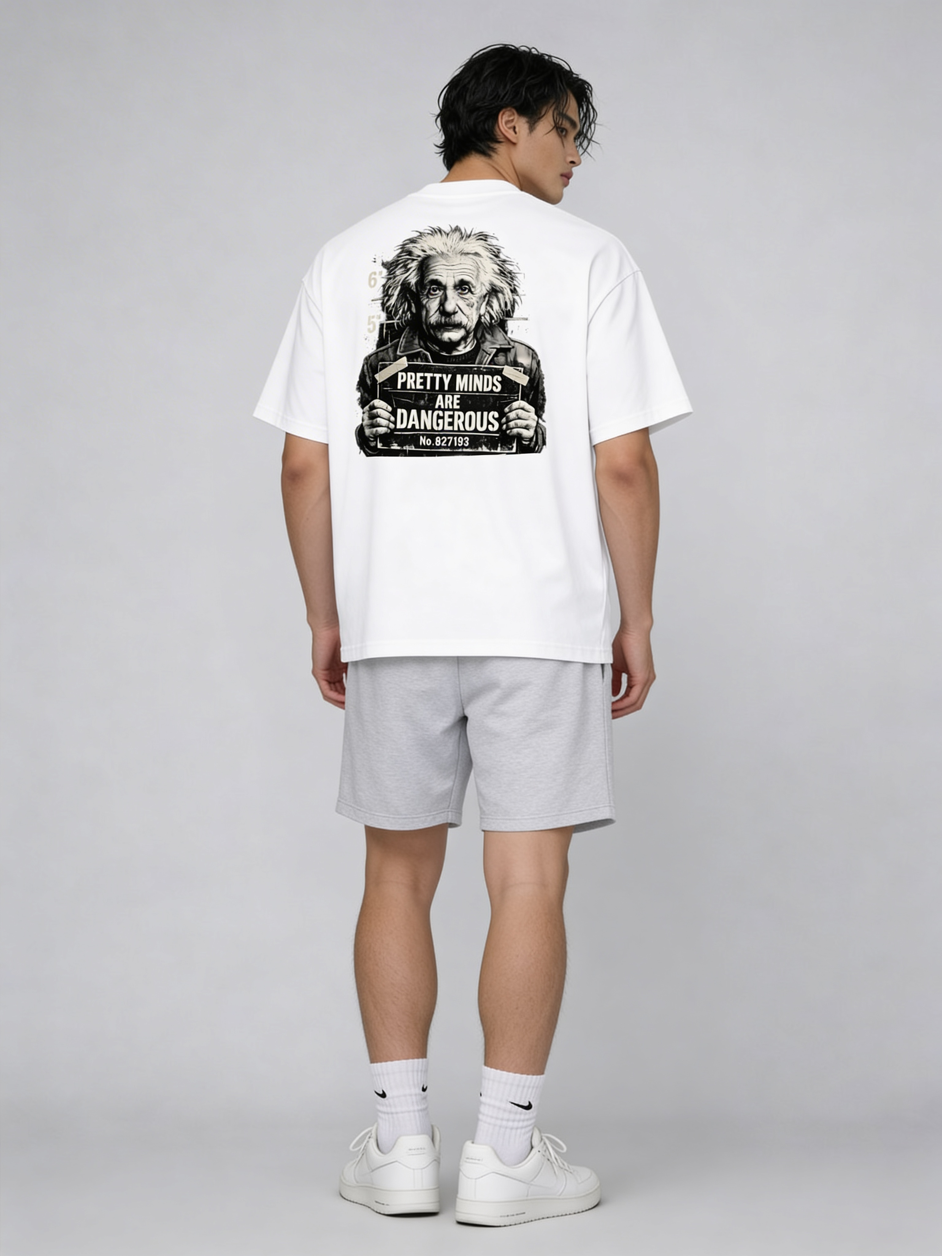 Young male model in oversized white graphic tee featuring Albert Einstein mugshot and “Pretty Minds Are Dangerous” statement on back, modern urban streetwear studio shot