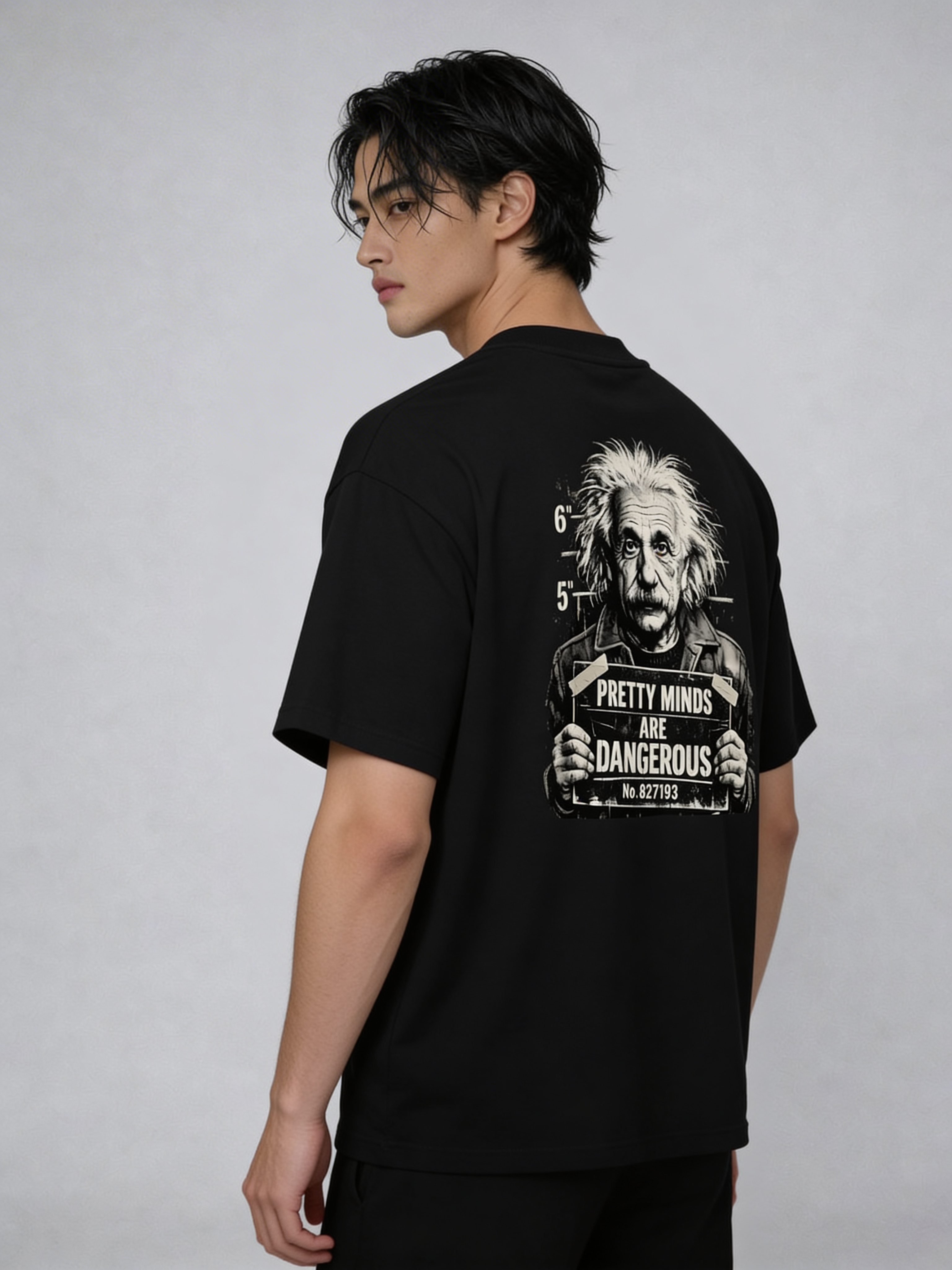 Male model wearing oversized black streetwear t-shirt with Albert Einstein mugshot design and bold “Pretty Minds Are Dangerous” back print, contemporary men’s fashion look
