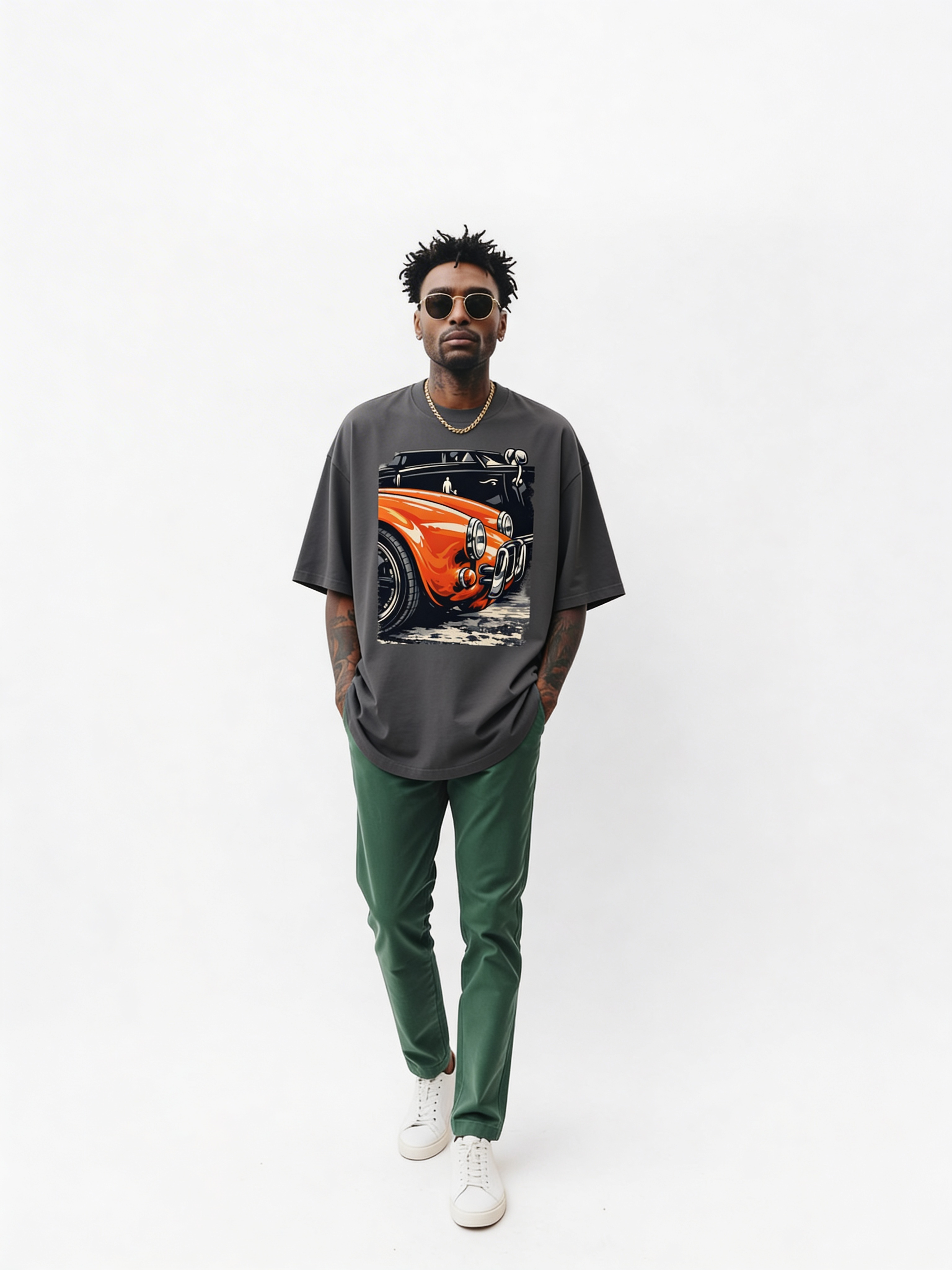 Male model walking in oversized grey streetwear t-shirt featuring vintage orange classic car graphic print, styled with green trousers and white sneakers in minimalist studio