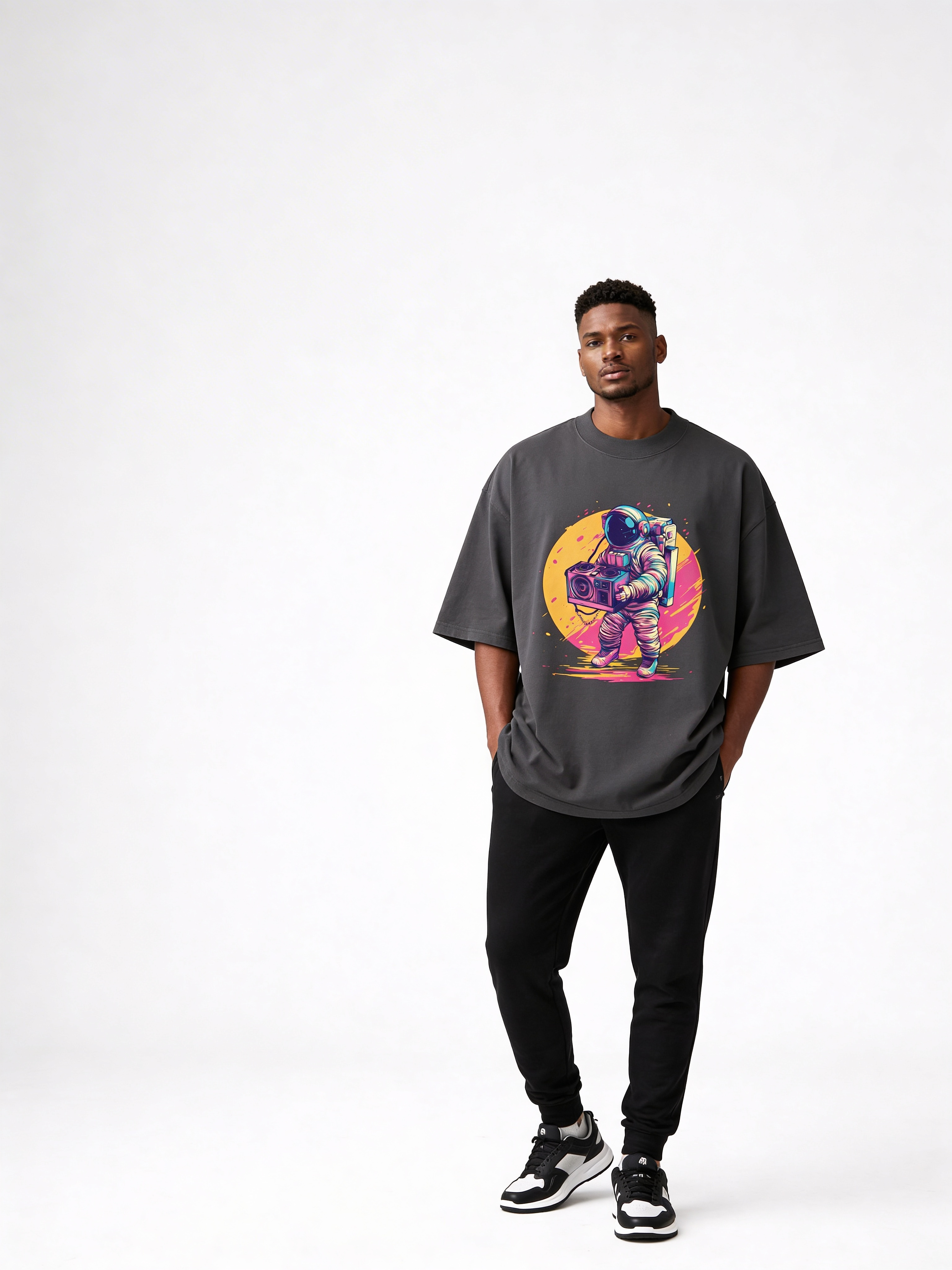 Male fashion model styled in oversized dark grey astronaut graphic t-shirt with black joggers and sneakers, minimalist studio streetwear outfit