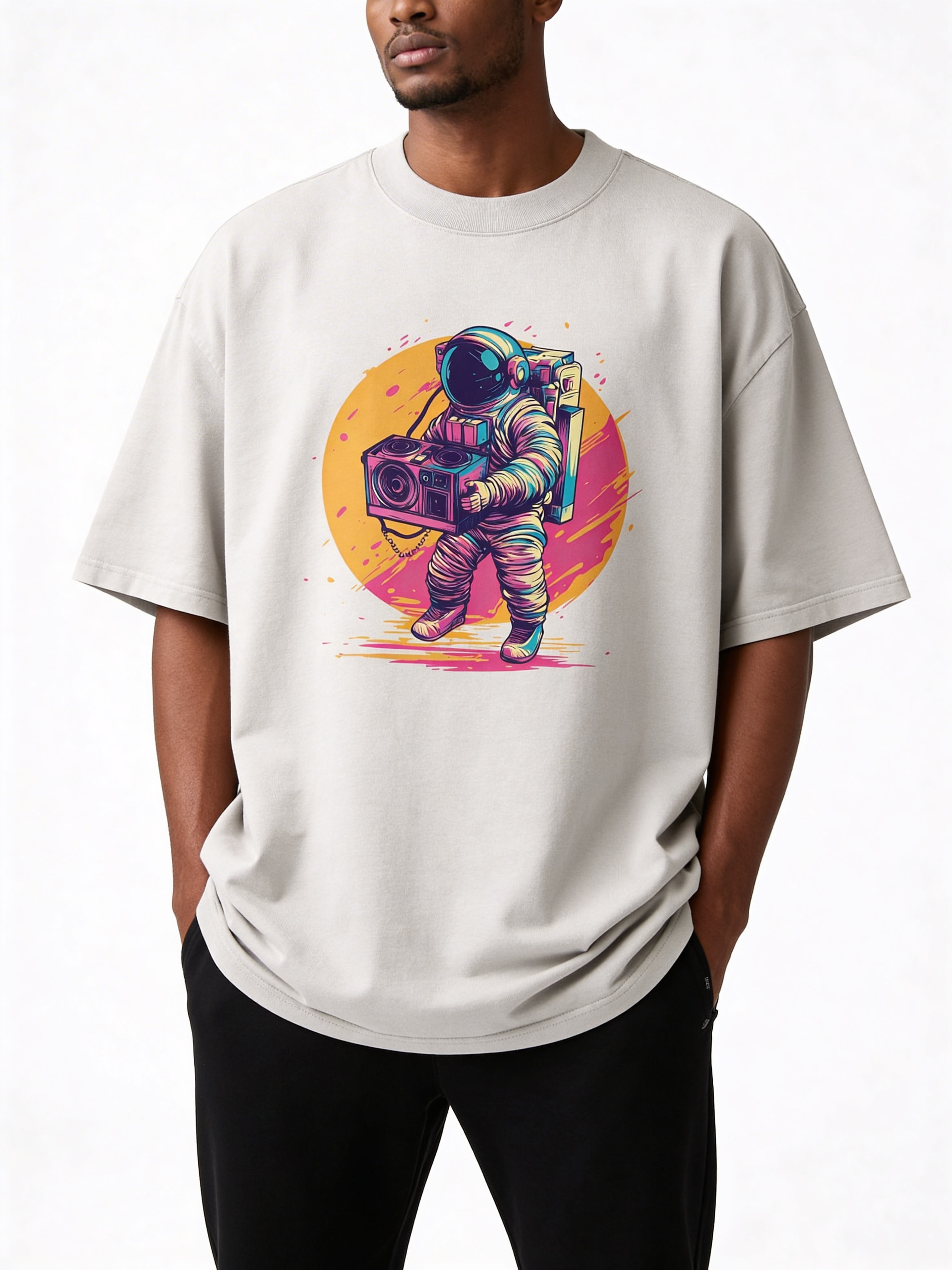 Male model wearing oversized beige streetwear t-shirt with colorful astronaut and boombox print on front, relaxed modern men’s fashion look