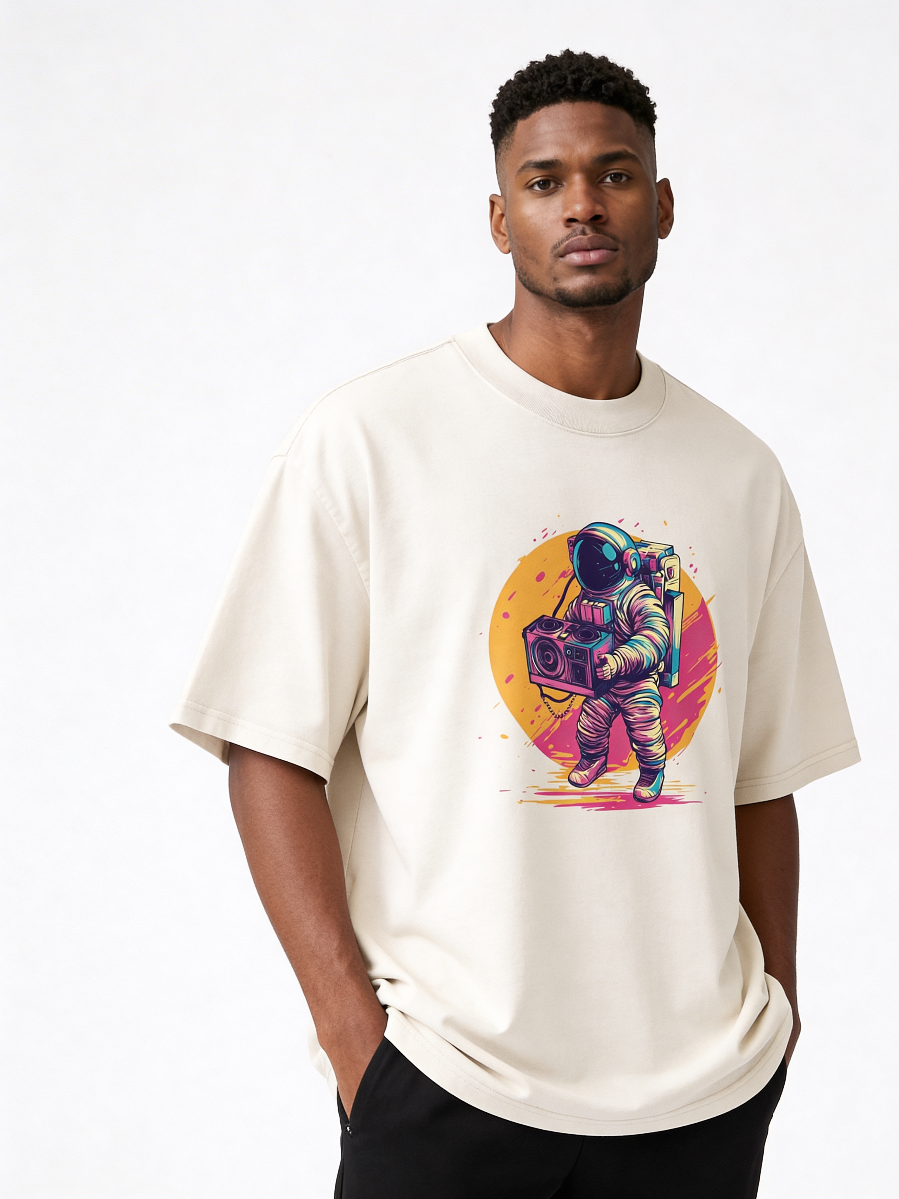 Male model posing in oversized beige graphic tee featuring neon astronaut illustration, paired with black pants for contemporary urban streetwear style