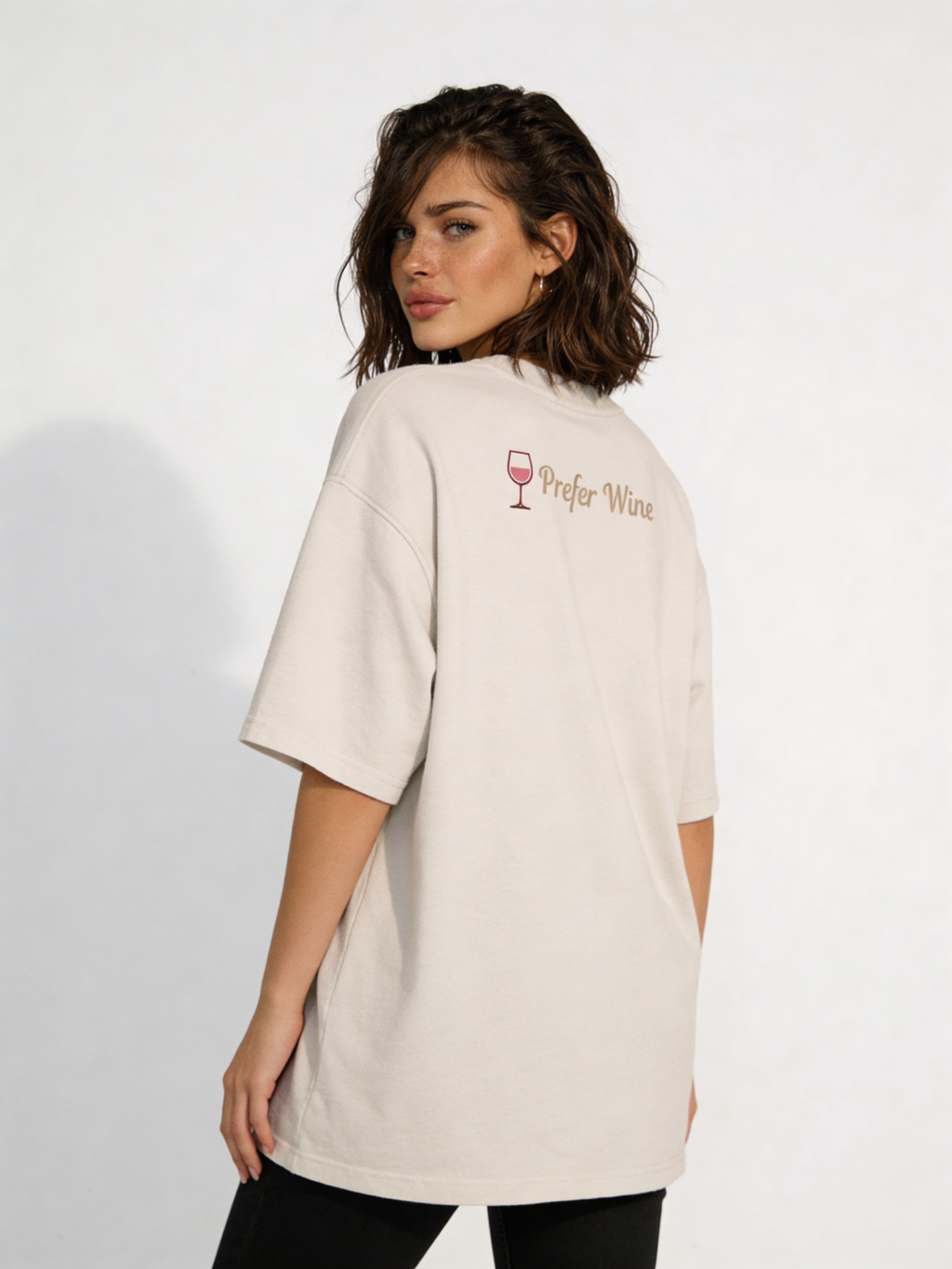 Female model showing back of oversized beige Valentine t-shirt with subtle “Prefer Wine” text and wine glass graphic, contemporary women’s streetwear look