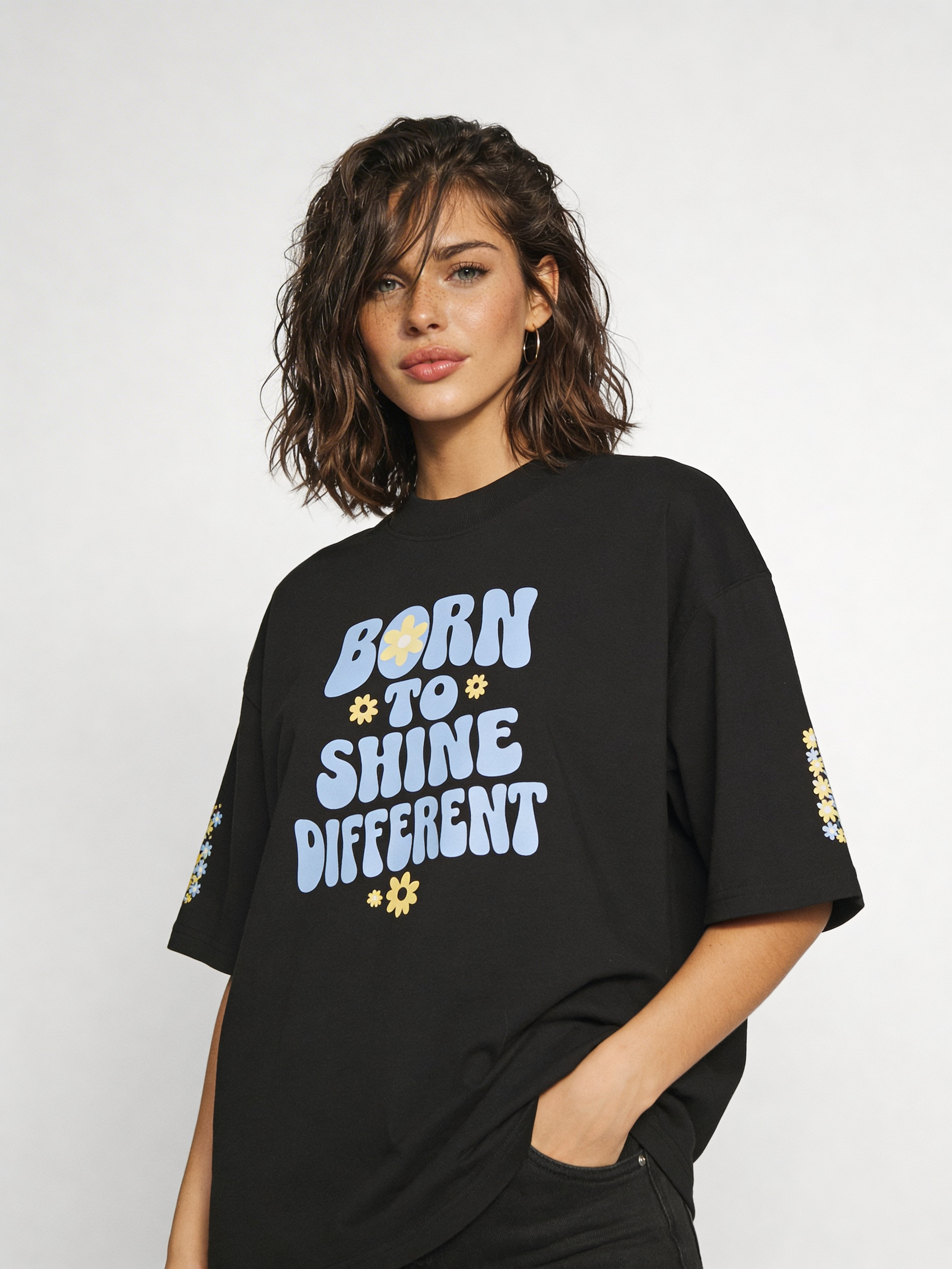 Female model wearing oversized black graphic t-shirt with “Born to Shine Different” quote and floral print, modern women’s streetwear look