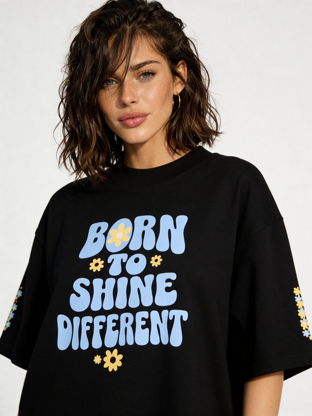 Close-up of black oversized women’s tee featuring “Born to Shine Different” pastel typography and flower graphics, contemporary casual fashion