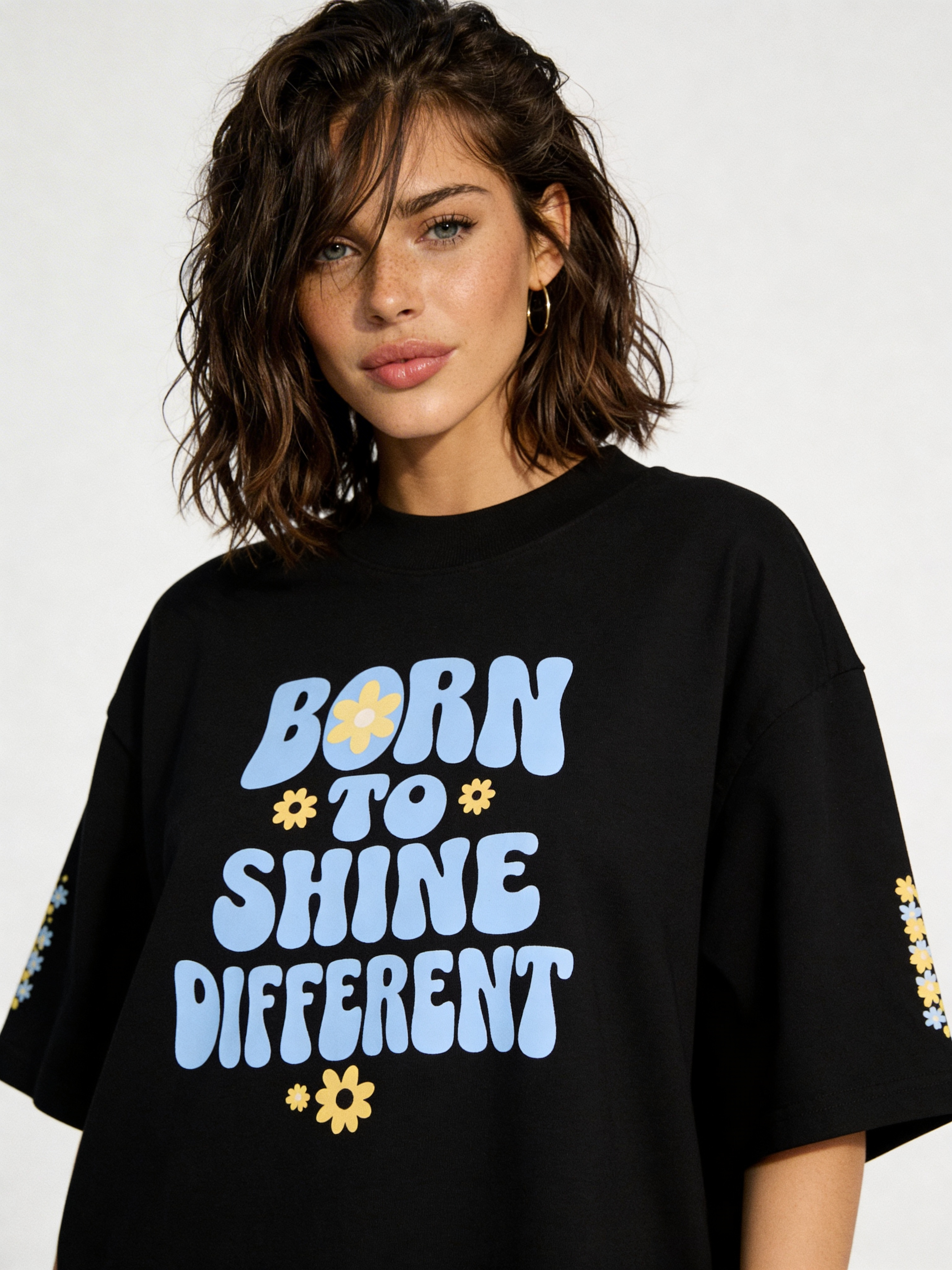 Close-up of black oversized women’s tee featuring “Born to Shine Different” pastel typography and flower graphics, contemporary casual fashion