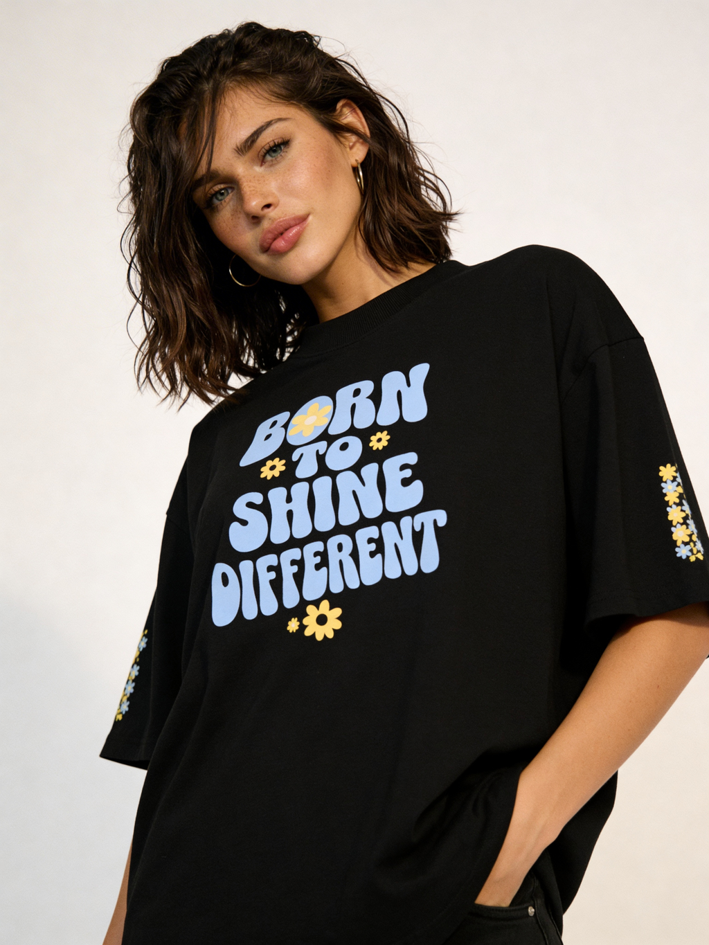 Female fashion model posing in oversized black motivational quote t-shirt with blue lettering and yellow floral details, relaxed streetwear style