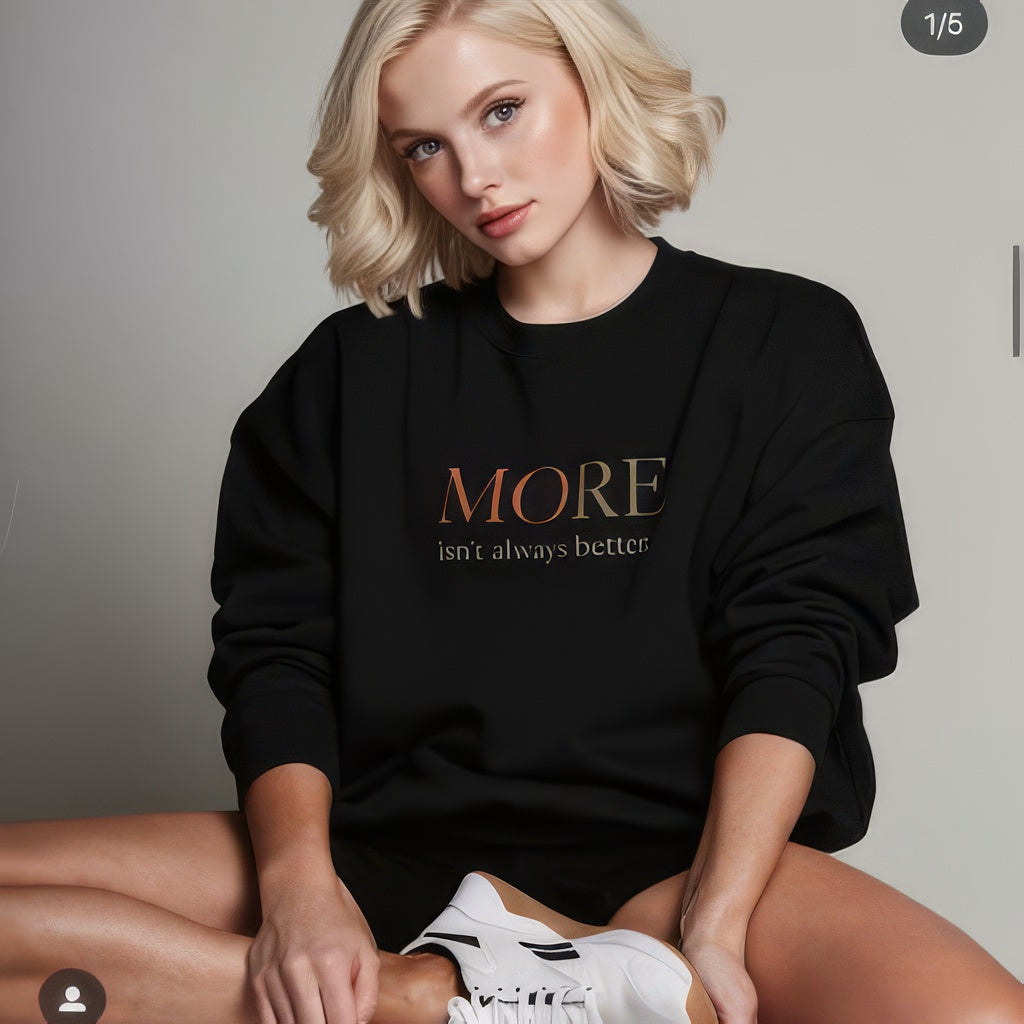 Female model wearing black oversized heavyweight sweatshirt with “MORE Isn’t Always Better” statement, artistic streetwear style