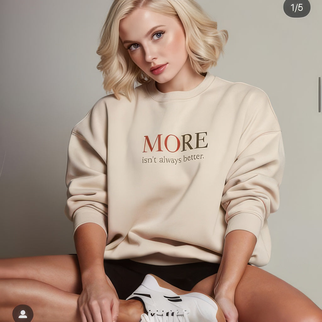 Female model wearing beige oversized heavyweight sweatshirt with “MORE Isn’t Always Better” message, minimalist streetwear look