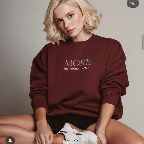 Female model wearing burgundy oversized heavyweight sweatshirt with “MORE Isn’t Always Better” typography, modern streetwear outfit