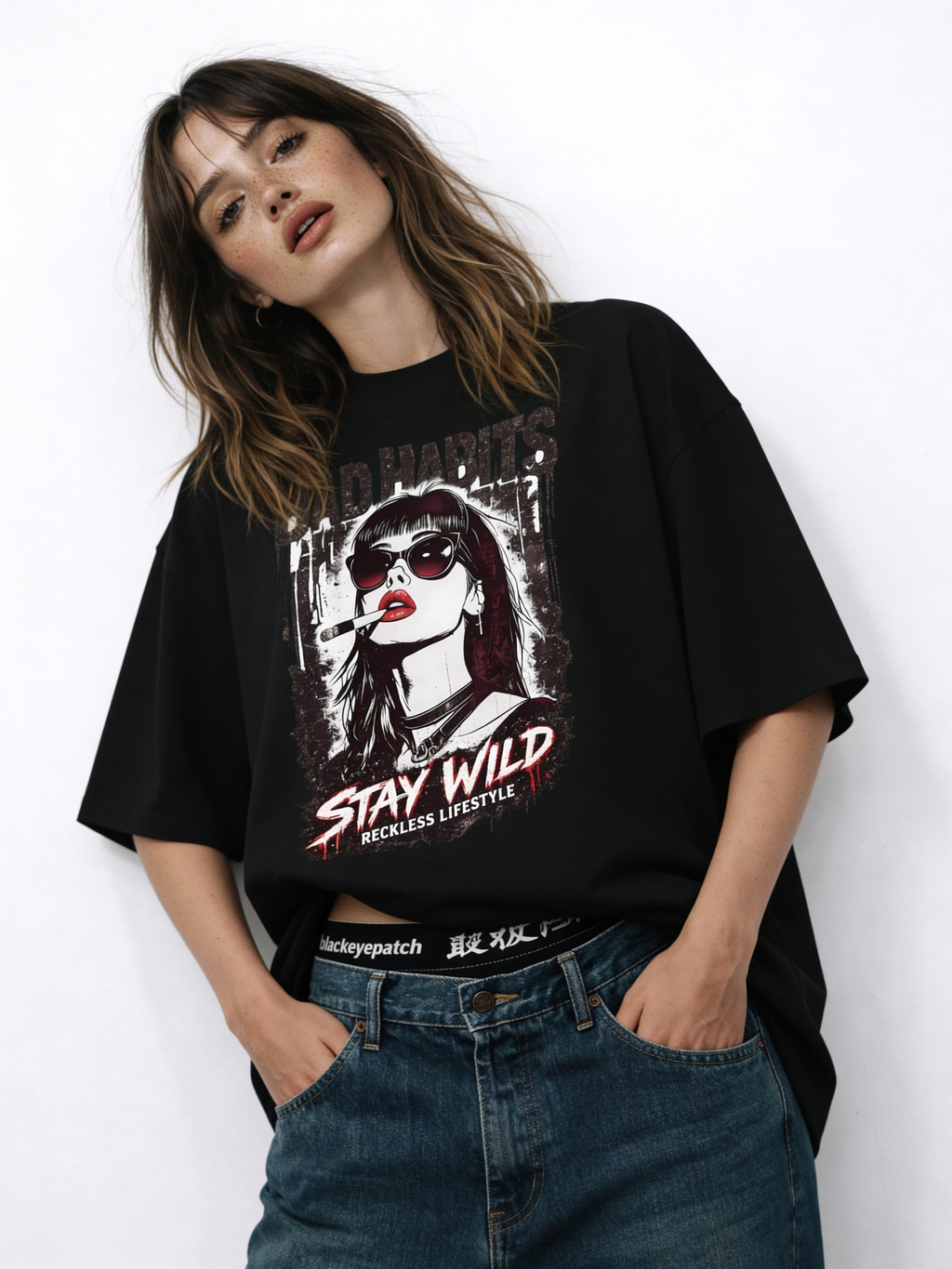 Woman modeling oversized black “Bad Habits Stay Wild” streetwear graphic t-shirt featuring rebellious illustrated portrait and bold red typography