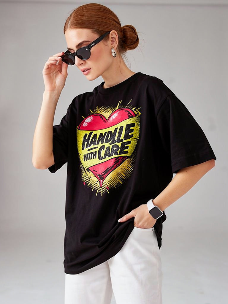 Model wearing black unisex t-shirt with “Handle With Care” heart graphic design in a studio setting