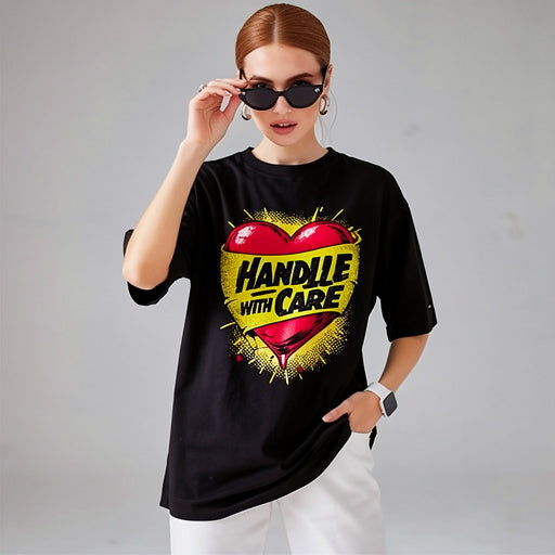 Model wearing black unisex t-shirt with “Handle With Care” heart graphic design in a studio setting