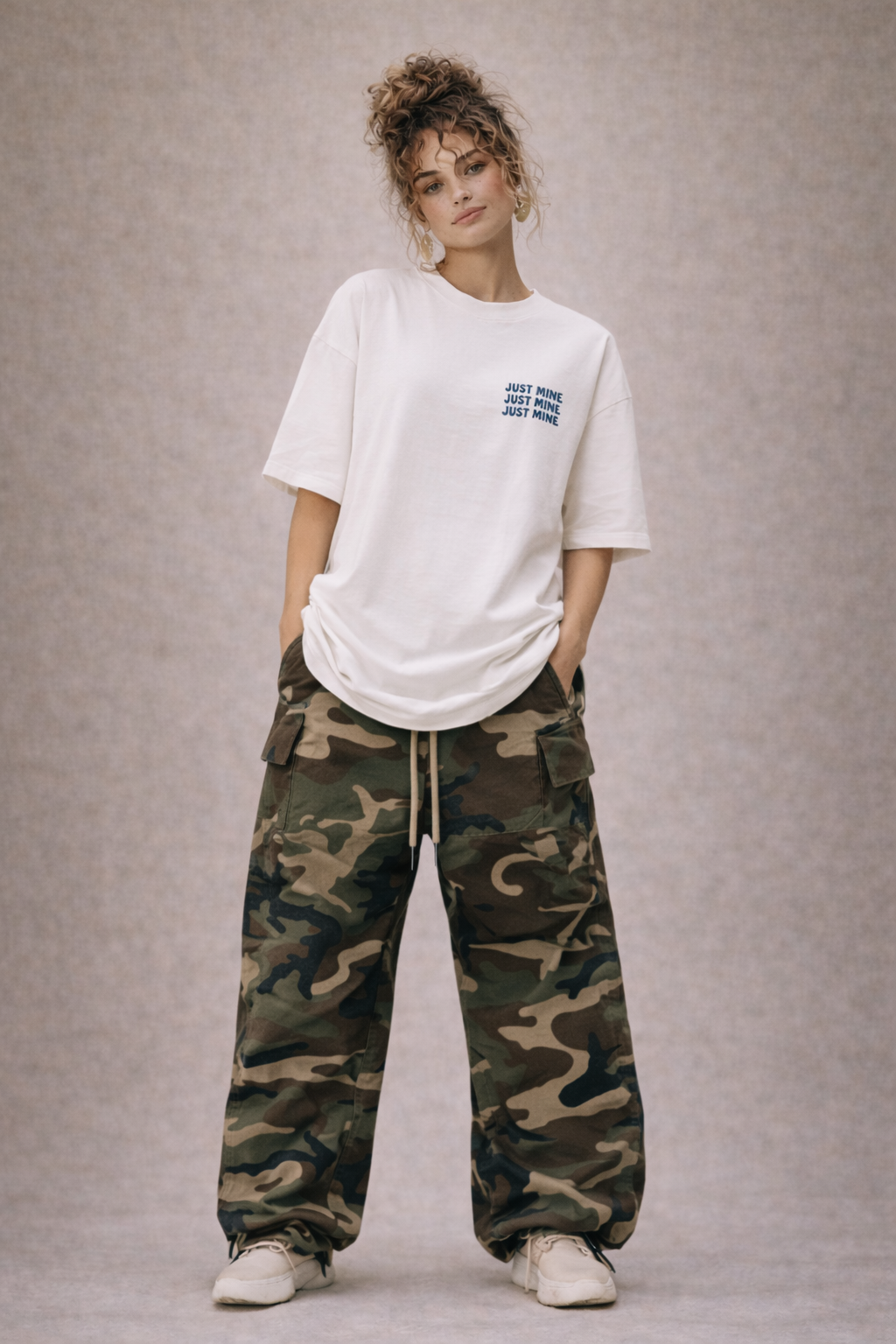 Full body view of woman wearing white oversized “Just Mine” graphic t-shirt with camouflage cargo pants, contemporary women’s streetwear style.