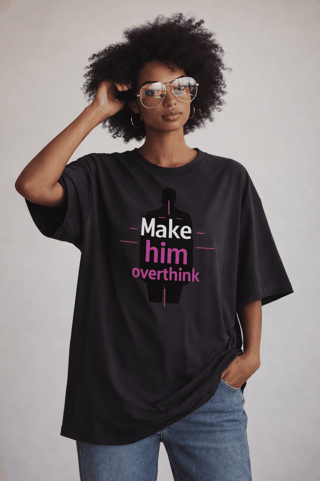 Female model in black oversized “Make him overthink” statement t-shirt with pink graphic print, modern women’s streetwear outfit.