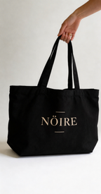 Black Nöiré graphic tote bag carried by hand, lifestyle view