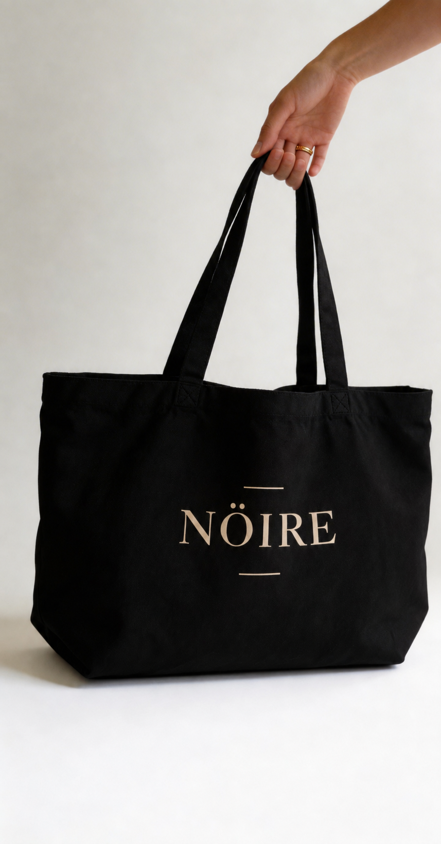 Black Nöiré graphic tote bag carried by hand, lifestyle view