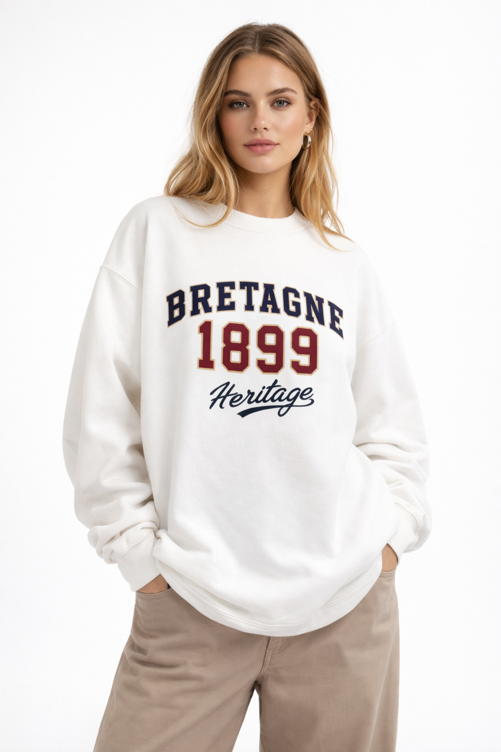 Woman in cream oversized “Bretagne 1899 Heritage” graphic sweatshirt with classic collegiate design, styled with beige pants, contemporary casual fashion.