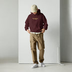 Model wearing maroon unisex hoodie with “No prayers needed just purpose” text design in a clean studio setting